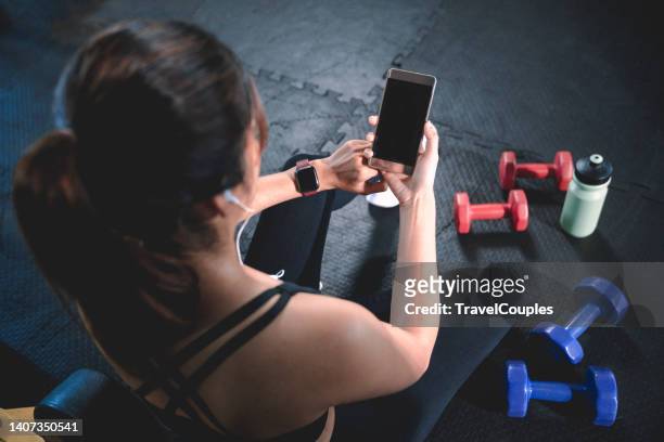 young woman with heart-rate or smart watch and smartphone in gym. sporty woman listening to music on smartphone in gym. tracking fitness application technology. healthy joyful sporty lifestyle. - running gear stock pictures, royalty-free photos & images