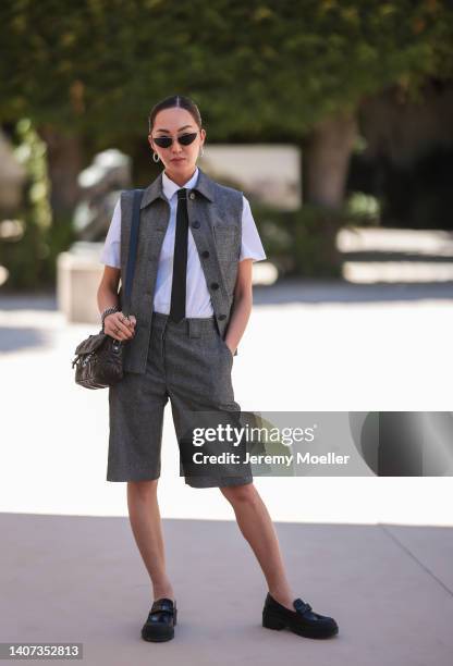 Chriselle Lim seen wearing black cat eyes sunglasses, silver earrings, a white short sleeves shirt, a black tie, a grey sleeveless / buttoned gilet...