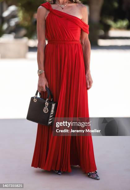 Guest seen wearing a flower diamonds necklace, a red asymmetrical one-shoulder pleated long dress, diamonds bracelet, a black shiny leather Lady Dior...