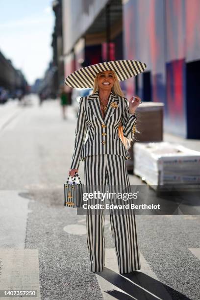 Guest wears a black and white striped print pattern oversized hat from Schiaparelli, a matching black and white striped print pattern with gold...