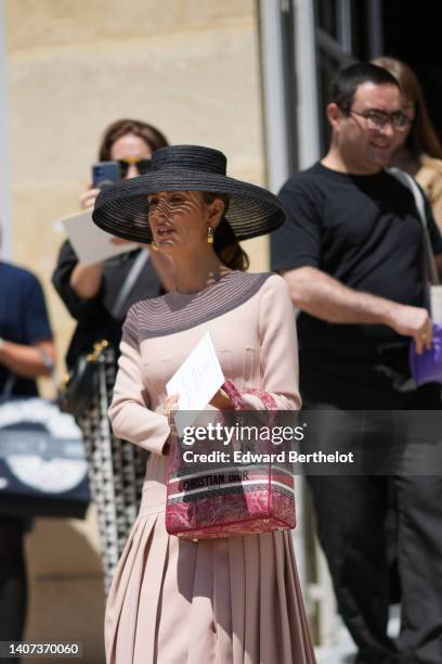 Guest wears a black wicker hat, gold earrings, a pale pink long sleeves / pleated dress from Dior, a white and pink print pattern Lady D-Lite hand...