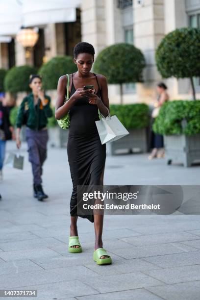 Guest wears a black V-neck / slit long midi tube dress, a green shiny leather shoulder bag, green shiny varnished leather platform soles mules /...