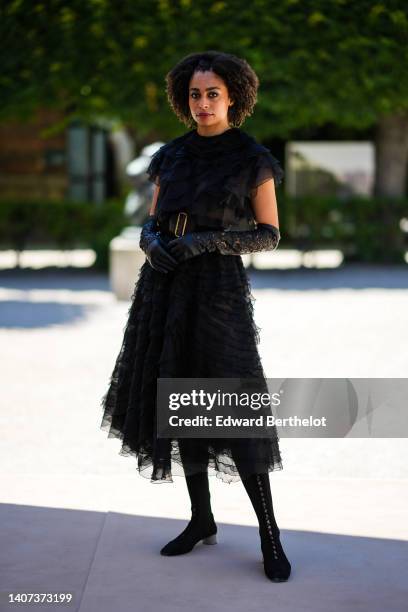 Guest wears a black ruffled tulle pleated / short sleeves / midi dress, a black shiny leather belt, black shiny leather cut-out pattern high gloves,...