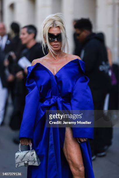 Guest seen wearing black large sunglasses from Balenciaga, a blue satin off-shoulder pleated / belted / oversized dress, a silver rhinestones logo...