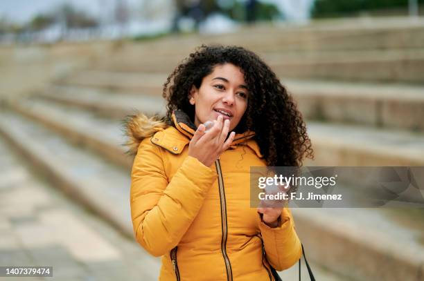 woman putting on lip protection in the street - lip balm stock-fotos und bilder