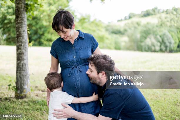 husband kisses his pregnant wife's belly while the older son hugs his mother's belly. - chilean ethnicity stock pictures, royalty-free photos & images
