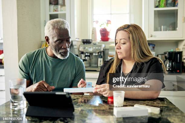 assistente domiciliare che consiglia il cliente senior sull'organizzazione delle pillole - contenitore organizer per pillole foto e immagini stock