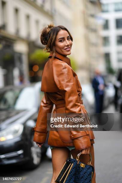 Tamara Kalinic wears a camel shiny leather shirt jacket from Fendi, a gold ring, a black and blue FF monogram print pattern handbag from Fendi, blue...