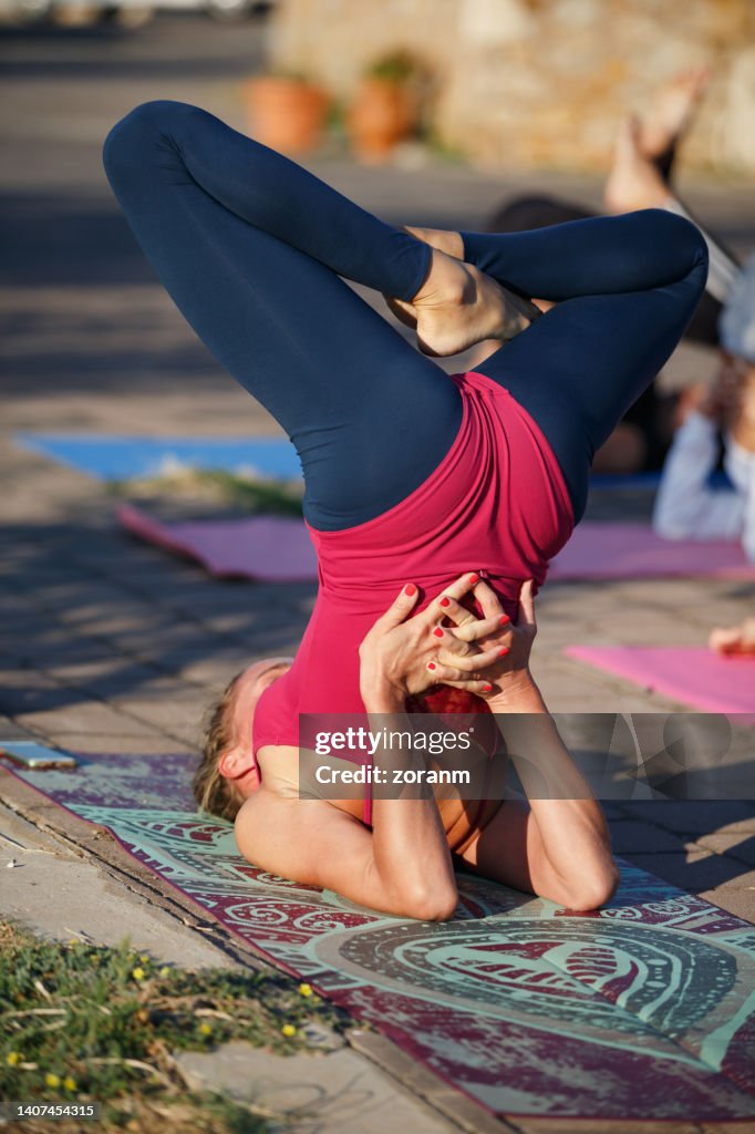 Instructor de yoga en clase con mujeres jóvenes, haciendo soporte de hombros con piernas en postura de loto