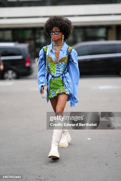 Sarah Monteil wears black and blue sunglasses, white large pendant earrings, silver large necklaces, a diamonds and a large emerald necklace, a blue...