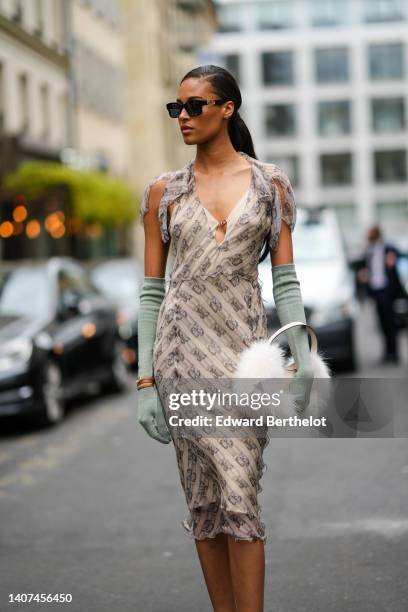 Cindy Bruna wears black sunglasses, a beige and brown monogram print pattern V-neck / short sleeves / silk knees dress from Fendi, pale green wool...