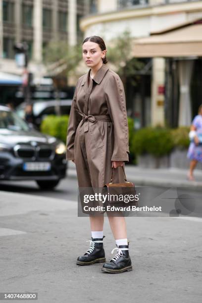 Guest wears silver earrings, a pink hair clip, a white pearls necklaces, a silver necklace, a brown oversized belted long trench coat, a brown suede...