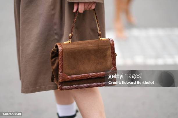 Guest wears a brown oversized belted long trench coat, a brown suede and leather snake pattern borders handbag, white socks, outside Fendi, during...