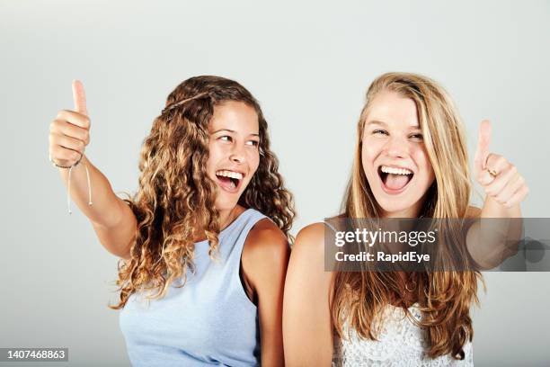 二人の美しい若者が微笑み、笑い、親指を立てるサインをする - happy woman thumbs studio ストックフォトと画像