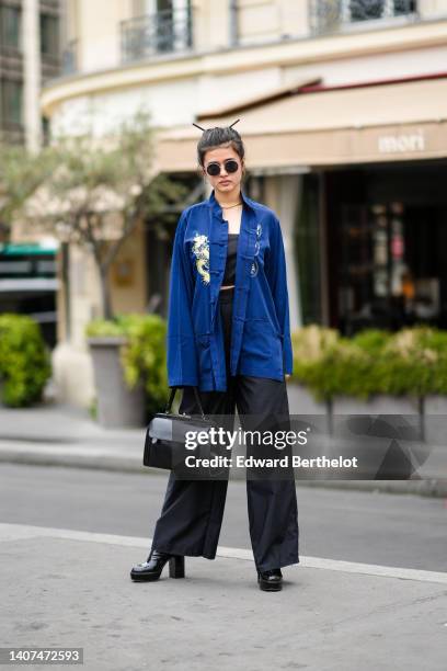 Guest wears black circle sunglasses, gold earrings, a gold necklace, a navy blue with embroidered pale yellow dragon print pattern kimono shirt, high...