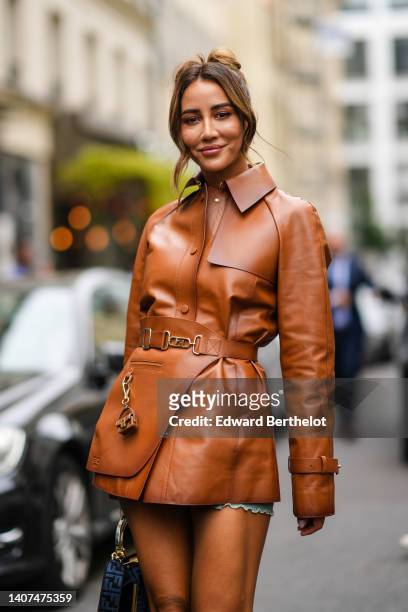Tamara Kalinic wears a camel shiny leather shirt jacket from Fendi, a gold ring, a black and blue FF monogram print pattern handbag from Fendi, blue...