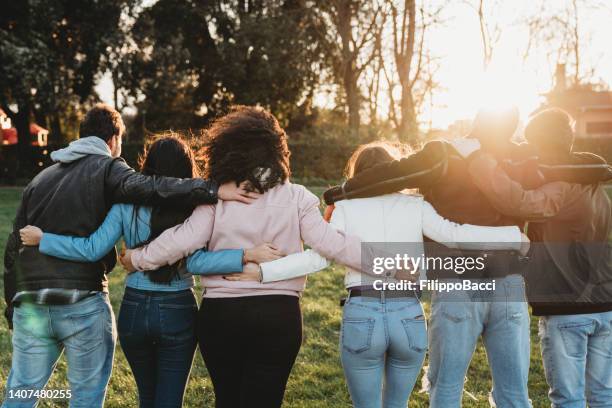 group of six teenager friends embracing together at the park, rear view - community arm in arm stock pictures, royalty-free photos & images