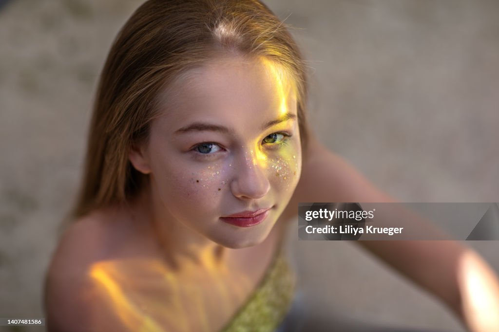 Beautiful young girl with glitter on her face and yellow reflections looks at the camera.