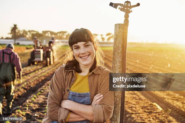 young proud female farmer leaning against the sprinkler pole in the field with arms crossed during a cultivation process. 
a happy beautiful lady framer with a smiling face standing on the farm. - farmer arms crossed stock pictures, royalty-free photos & images