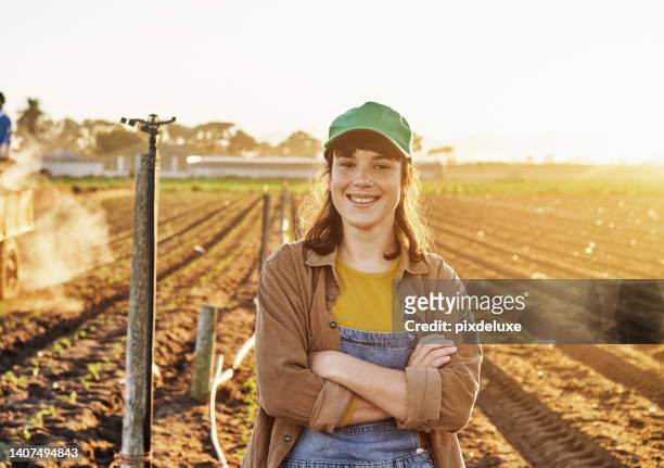 female organic farmer standing arms crossed in a field on her sustainable farm. a young agricultural worker smiling with arms folded. confident farmhand on open farmland during planting season - farmer arms crossed stock pictures, royalty-free photos & images