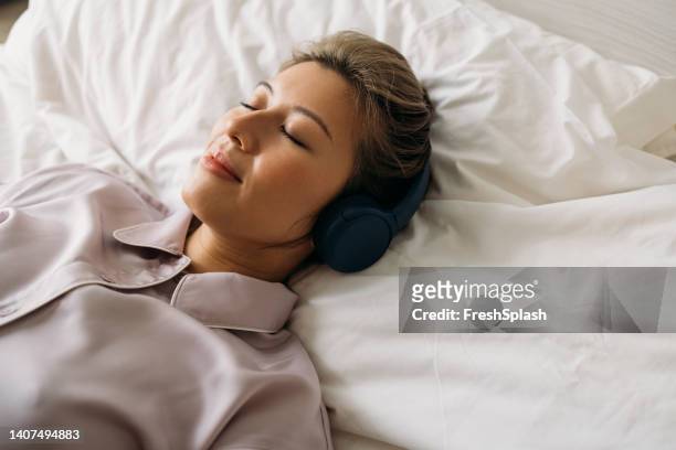 sound asleep: eine schöne lächelnde frau, die auf dem bett schläft, während sie musik hört - silk pillow stock-fotos und bilder