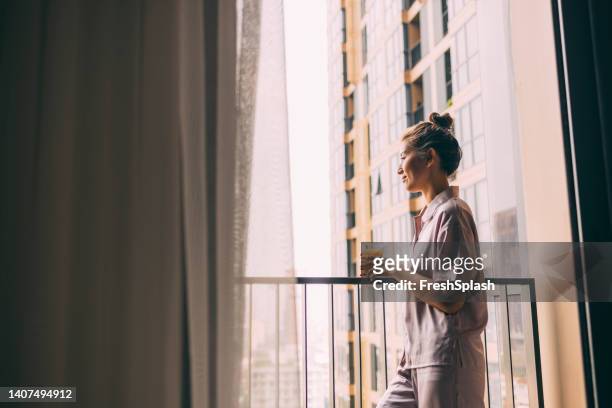 a beautiful smiling woman looking away while relaxing at home holding a glass of her favourite drink - silk pajamas stock pictures, royalty-free photos & images
