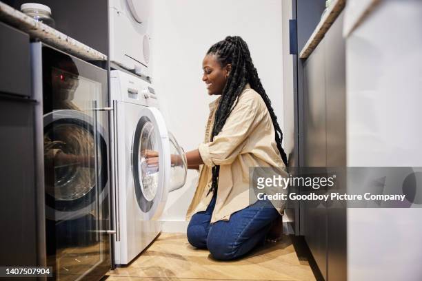 smiling young woman doing the laundry in a utility room at home - utility room stock pictures, royalty-free photos & images