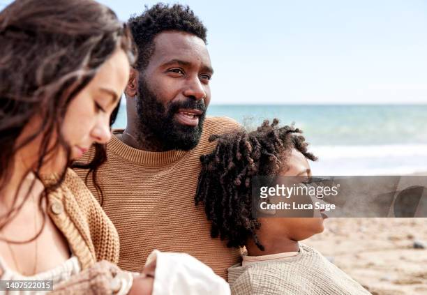 a relaxed thoughtful moment on the beach for a father and his eldest son and partner and baby daughter - beach black and white stock pictures, royalty-free photos & images