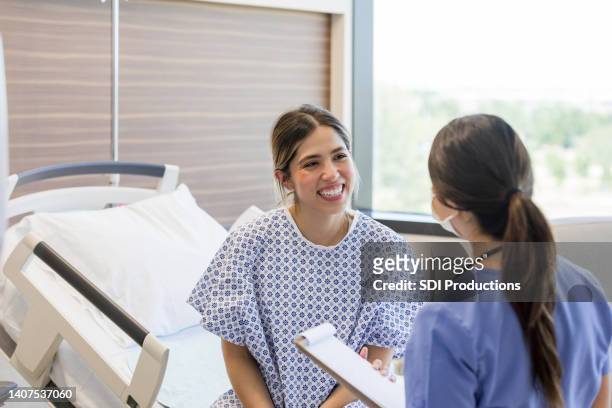 junge erwachsene patientin erhält gute nachrichten von krankenschwester - spitalbett stock-fotos und bilder