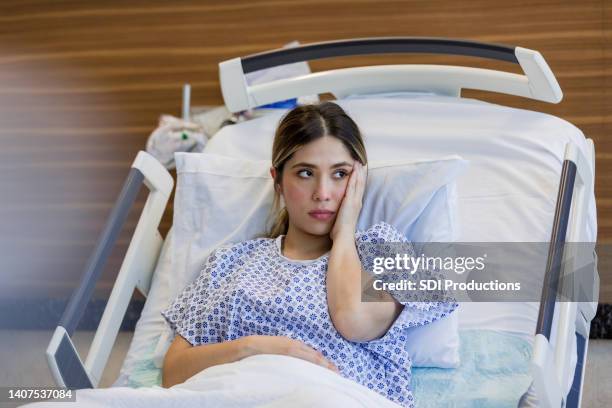 sad young adult woman in hospital puts hand to face - er stock pictures, royalty-free photos & images