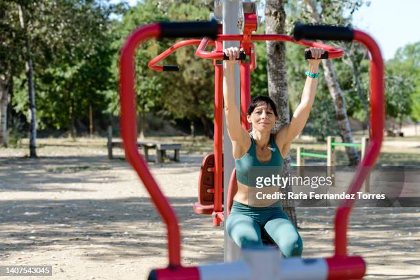young athletic woman working out on workout ground with exercise equipment outdoor - trainingsmaschine stock-fotos und bilder