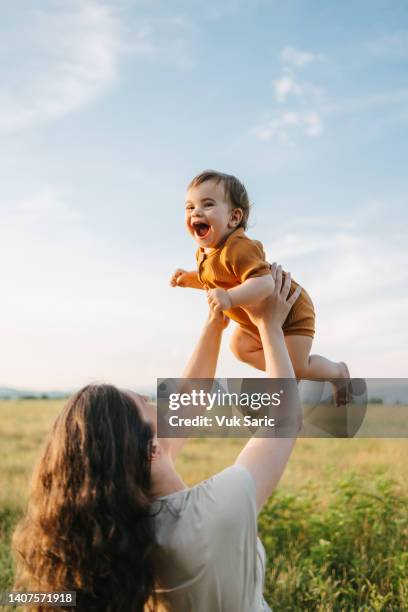 mama hält ihr baby am himmel hoch - eltern baby hochheben stock-fotos und bilder