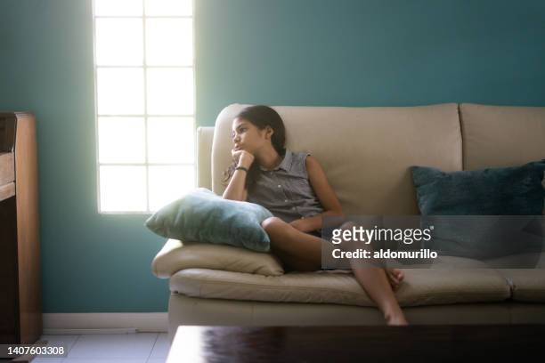 niña aburrida sentada en el sofá de casa y mirando hacia otro lado - psychiatrists couch fotografías e imágenes de stock