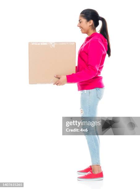 generation z female in front of white background wearing canvas shoe and holding cardboard box - side view carrying stock pictures, royalty-free photos & images