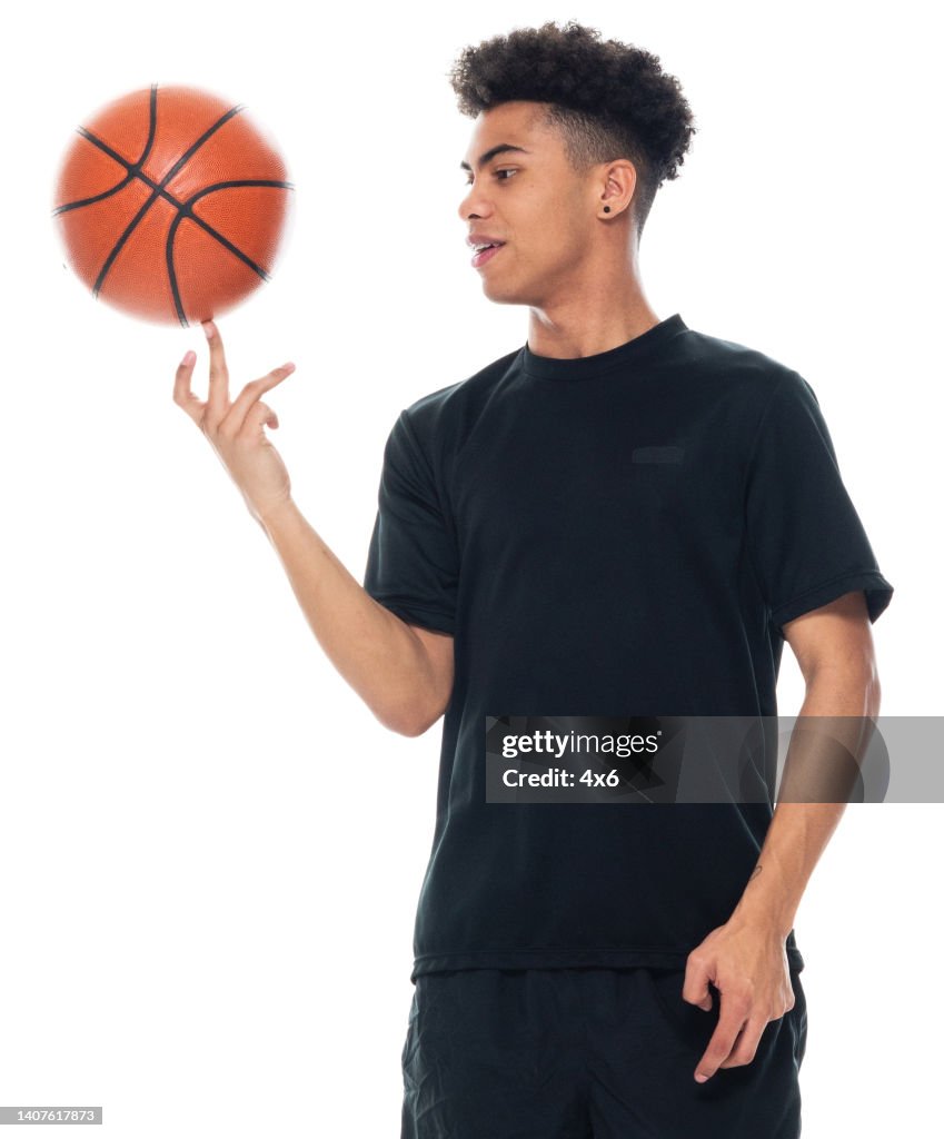 African ethnicity young male spinning in front of white background wearing sports clothing and holding basketball - ball and using sports ball