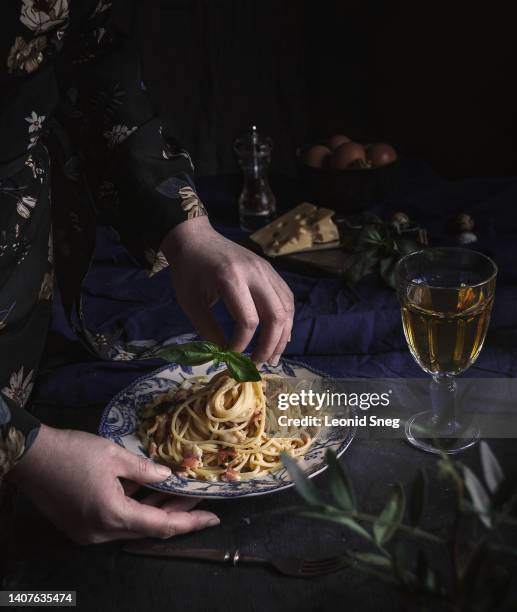 woman serving plate with spaghetti carbonara on dark background - carbonara sauce stock pictures, royalty-free photos & images