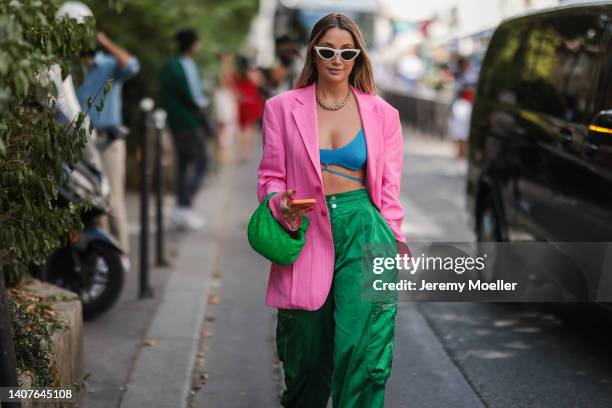 Guest wears white latte sunglasses, a pink linen oversized blazer jacket, gold earrings, a gold large chain necklace, a blue ribbed wool V-neck laces...