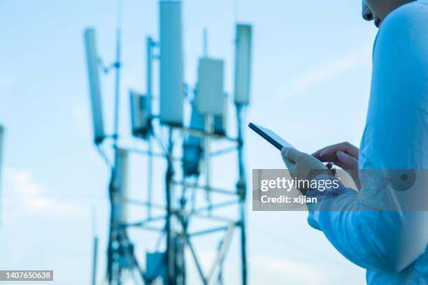 mano umana che utilizza il telefono cellulare vicino alla torre di comunicazione 4g, 5g - torre di trasmissione a microonde foto e immagini stock
