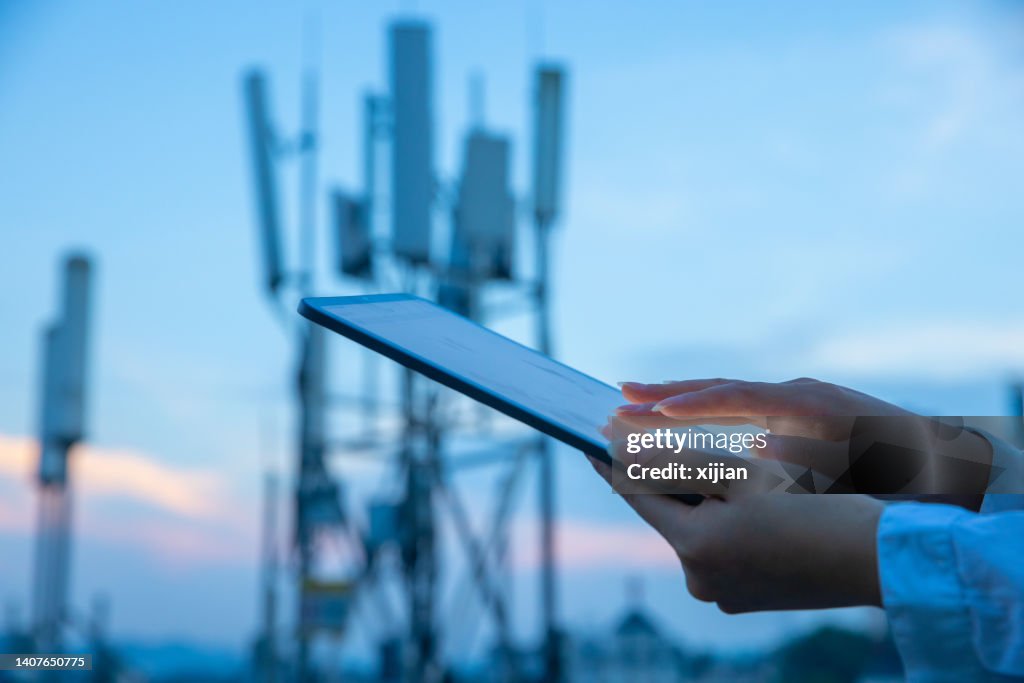Human hand using digital tablet near 4G,5G communications tower