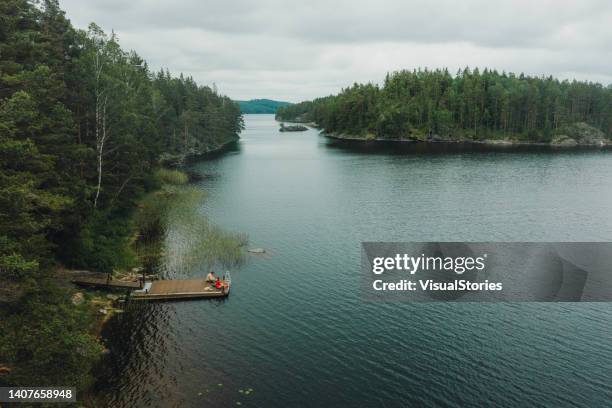 scenic aerial view of woman and man contemplating summer on the pier by the lake in the forest in sweden - huisje stockfoto's en -beelden