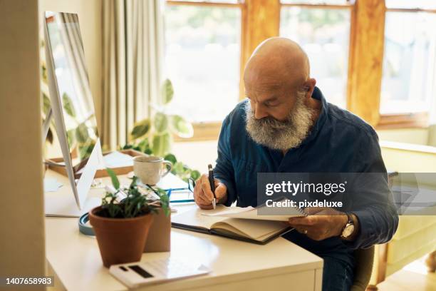 mature man writing in a notebook diary and sitting alone in a home bedroom. senior entrepreneur using paperwork and computer to calculate his finances. journaling poetry or planning business schedule - old diary stock pictures, royalty-free photos & images