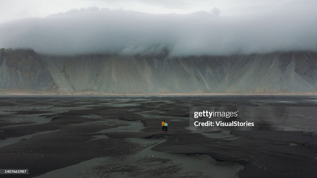 Luftaufnahme von Mann und Frau, die am malerischen Strand von Stokksnes mit Sanddünen in Island spazieren gehen
