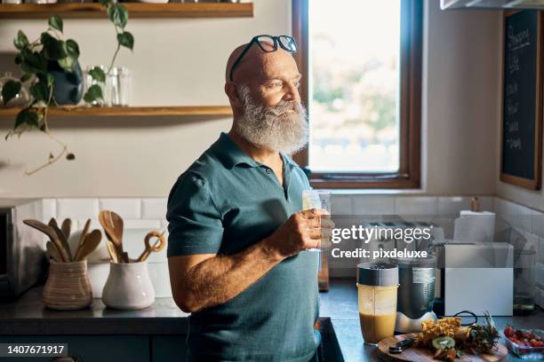 senior man drinking a healthy smoothy made with a blender. health conscious retiree having fresh organic juice. a daily routine drink of blended vegetables and fruits to improve health and wellbeing - proteïnedrank stockfoto's en -beelden