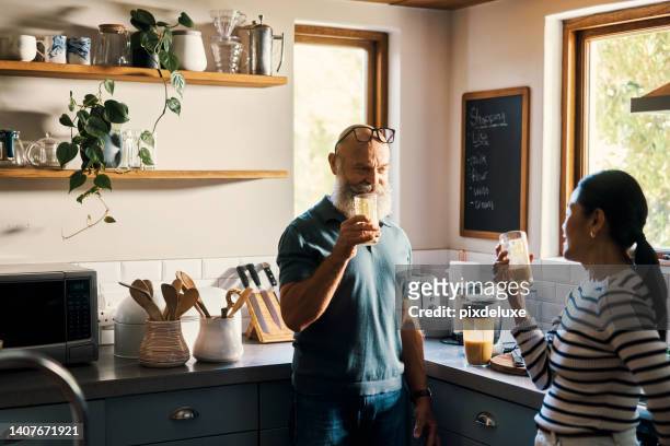 senior couple drinking healthy smoothies together in the kitchen at home. retired interracial husband and wife tasting a shake they made in the morning. mature man and woman enjoying a fresh snack - healthy food and drink stock pictures, royalty-free photos & images