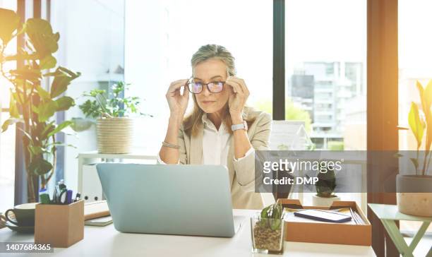 female boss networking with clients on the web. manager adjusting spectacles while reading and sending emails. mature business woman using laptop browsing online putting on her glasses at work. - adjusting stockfoto's en -beelden