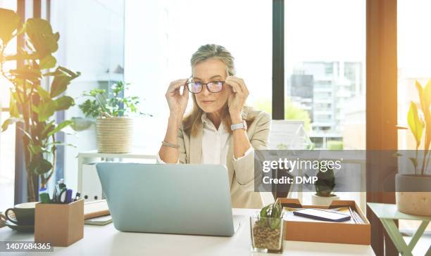 female boss networking with clients on the web. manager adjusting spectacles while reading and sending emails. mature business woman using laptop browsing online putting on her glasses at work. - adjusting bildbanksfoton och bilder