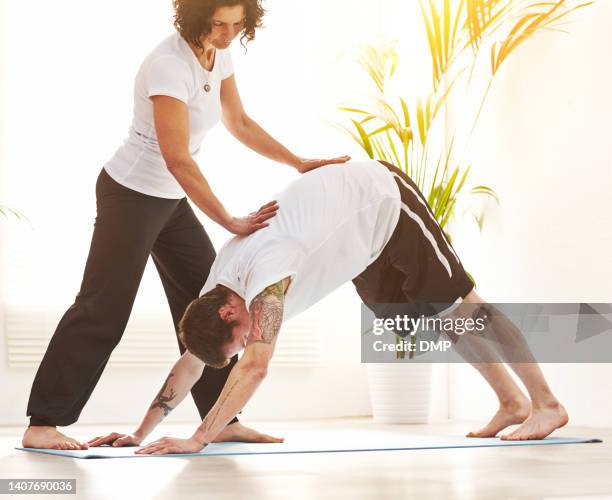 female yoga instructor training a man to do downward dog pose during a fitness class in an exercise studio. yogi helping to correct body form and posture during a pilates lesson with inversion asana - upright position stock pictures, royalty-free photos & images