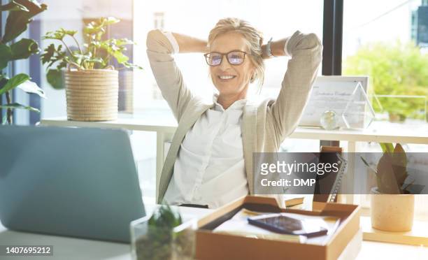 happy mature manager satisfied and relieved to be done with deadlines and tasks. business woman feeling accomplished and enjoying a relaxing break to stretch with hands behind her head in an office. - vrouw 50 jaar stockfoto's en -beelden