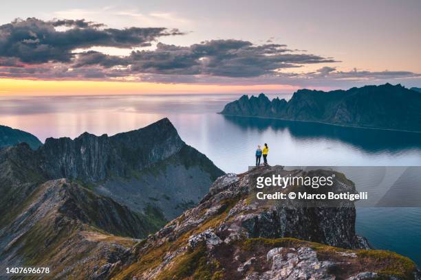 two friends admiring the sunset from top of a high cliff in northern norway - senderismo fotografías e imágenes de stock