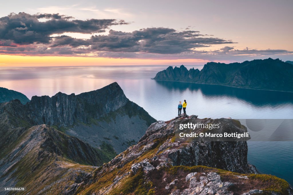 Two friends admiring the sunset from top of a high cliff in Northern Norway